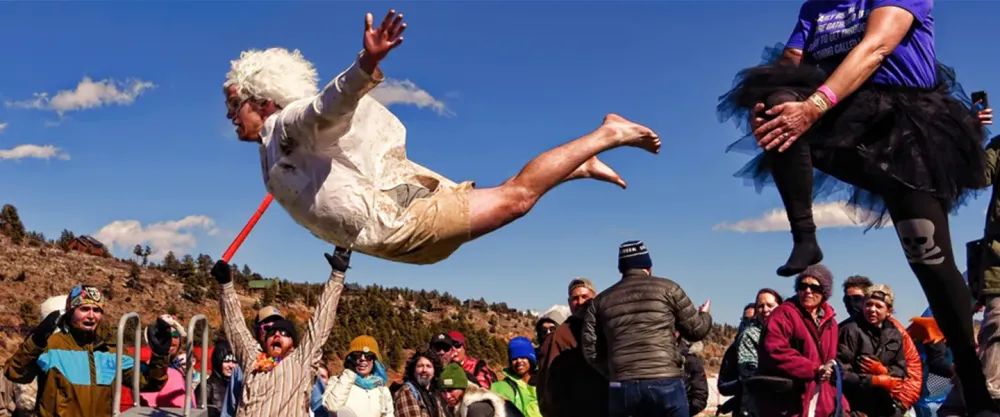 Man jumping from a platform while a crowd cheers on at Frozen Dead Guy Days festival